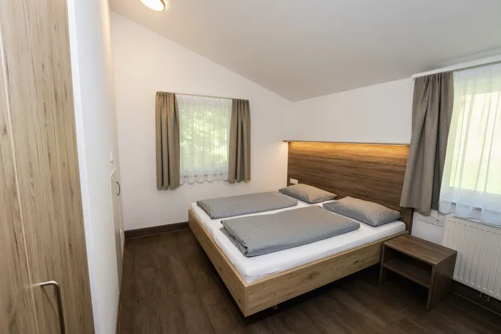 Gemütliches Schlafzimmer mit Doppelbett, Holzmöbeln und zwei Fenstern.