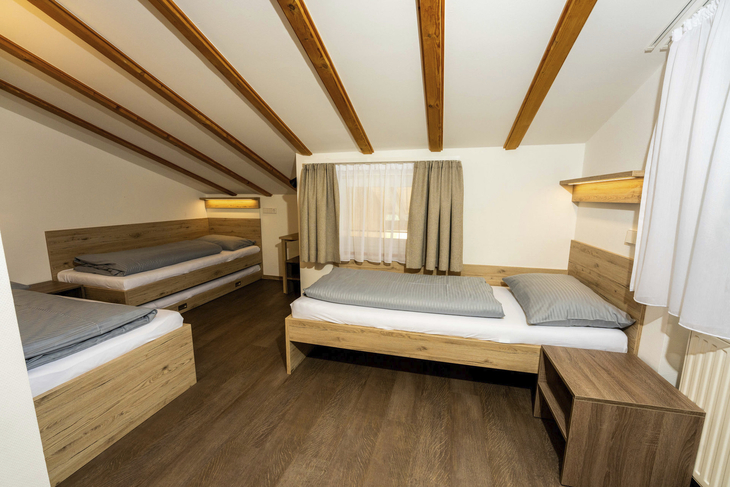 Dreibettzimmer mit Holzmöbeln und Tageslicht durch Fenster.