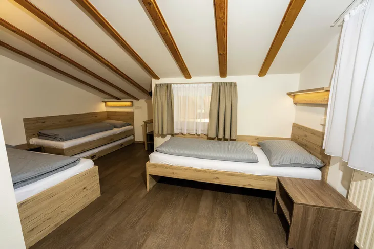 Dreibettzimmer mit Holzmöbeln und Tageslicht durch Fenster.