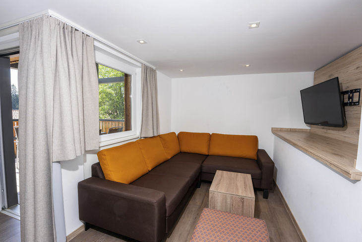 Wohnzimmer mit braun-oranger Couch, kleinem Tisch und Wandfernseher.