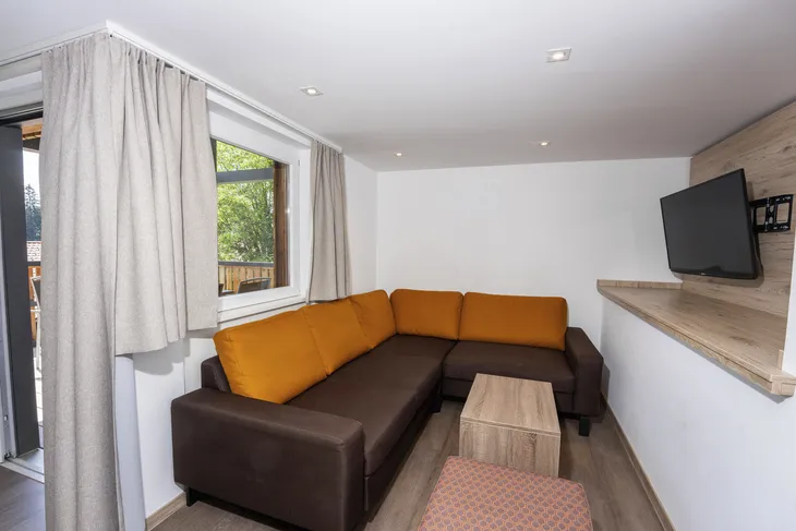Wohnzimmer mit braun-oranger Couch, kleinem Tisch und Wandfernseher.