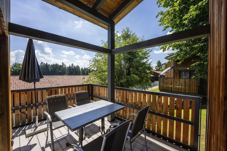 Holzveranda mit Tisch, Stühlen und Sonnenschirm im Grünen.