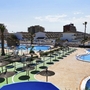 Aussicht auf Hotelpoolanlage mit Sonnenschirmen und umliegender Architektur bei sonnigem Wetter.