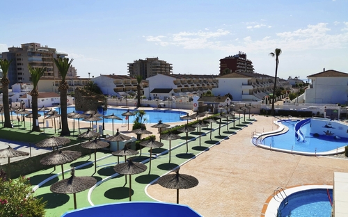 Aussicht auf Hotelpoolanlage mit Sonnenschirmen und umliegender Architektur bei sonnigem Wetter.
