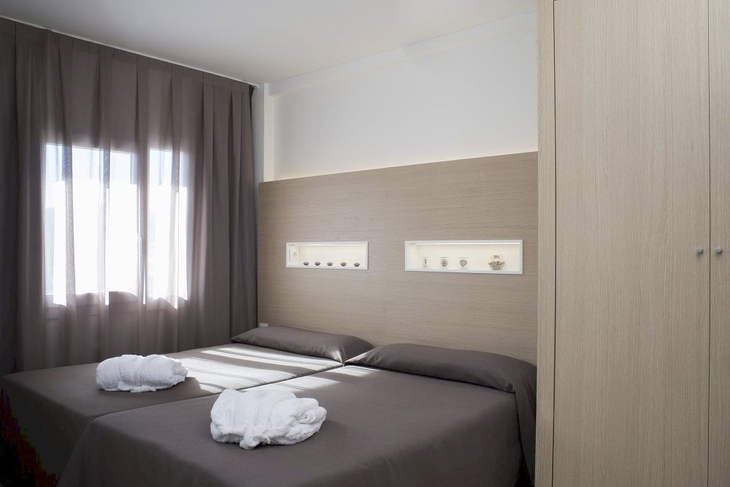 Helles Hotelzimmer mit zwei Einzelbetten und Vorhängen am Fenster.