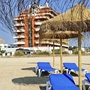 Sonnenliegen unter Strohdächern am Strand vor einem Hotel.