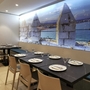 Restaurant mit gedeckten Tischen und Wandfoto von Meer und Mauer.