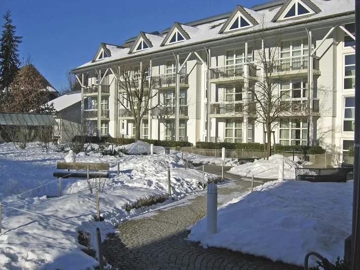 Mehrstöckiges Gebäude im Winter mit verschneitem Garten.
