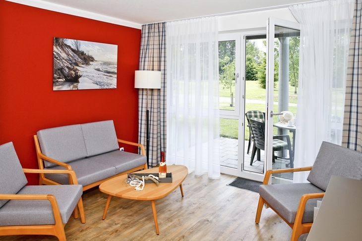 Wohnzimmer mit roten Wänden, grauen Möbeln und Balkon mit Gartenblick.