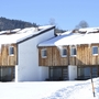 Verschneite Holzhäuser im Winter mit Eiszapfen am Dach.