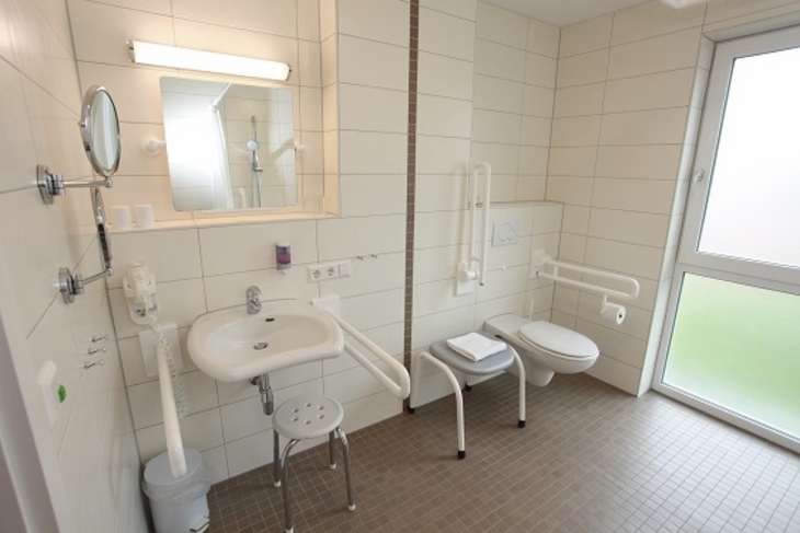Barrierefreies Badezimmer mit Waschbecken, Spiegel und Haltegriffen an der Wand.