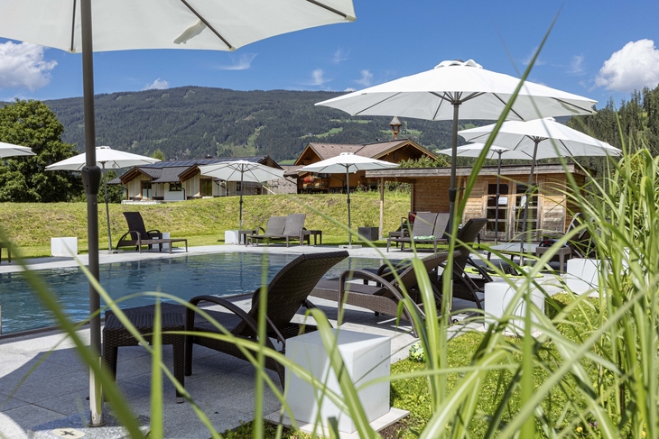 Pool mit Liegestühlen und Sonnenschirmen in bergiger Landschaft bei Radstadt.