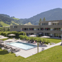 Gebäude mit Pool, Sonnenschirmen und grüner Hügellandschaft im Hintergrund.
