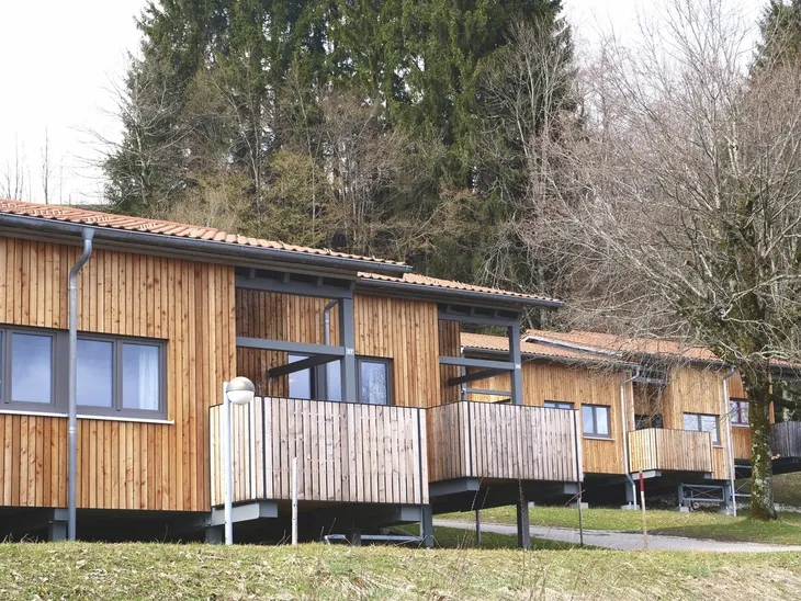 Reihenhäuser aus Holz mit Veranda in einer bewaldeten Umgebung.