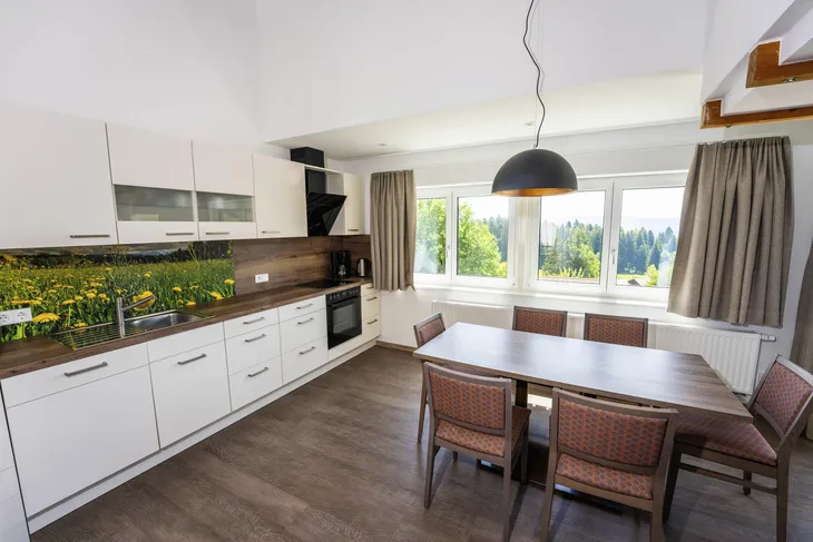 Moderne Küche mit Esstisch und großen Fenstern, Blick auf Bäume.