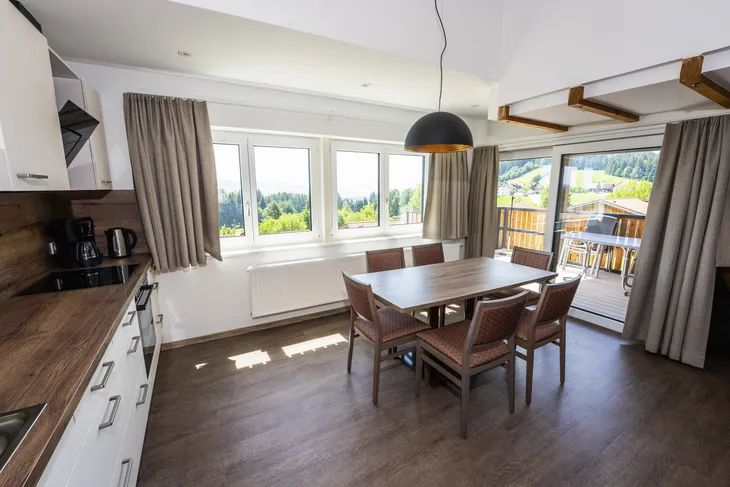 Essbereich in einer modernen Ferienwohnung mit großem Fensterausblick ins Grüne.