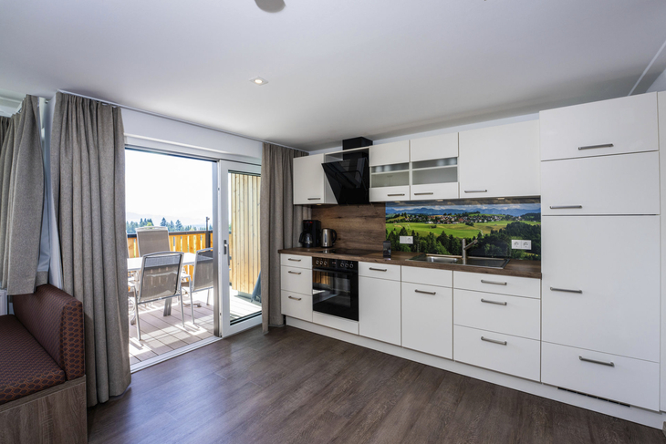 Helle Küche mit Balkon und Ausblick auf eine Landschaft.