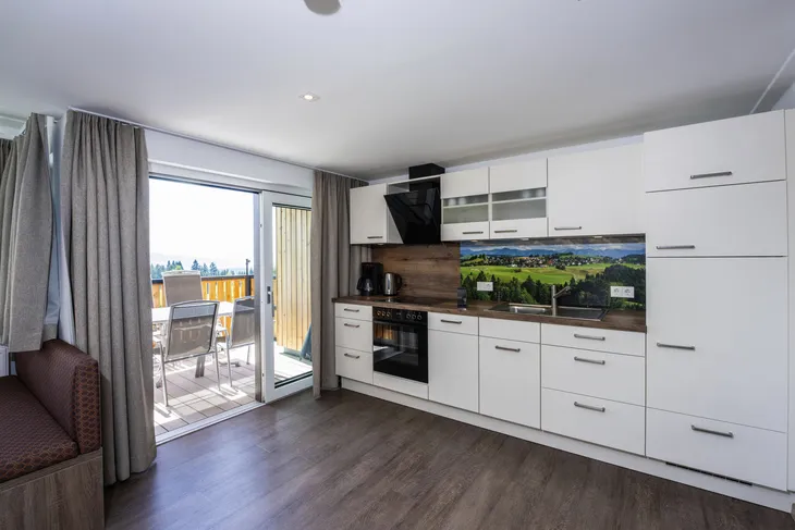Helle Küche mit Balkon und Ausblick auf eine Landschaft.