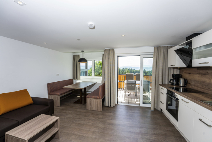 Moderne Ferienwohnung mit Küchenzeile und Essbereich, Blick auf Balkon und Landschaft.