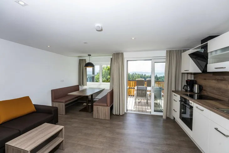 Moderne Ferienwohnung mit Küchenzeile und Essbereich, Blick auf Balkon und Landschaft.
