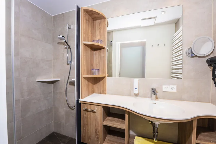 Modernes Badezimmer mit Waschtisch, Spiegel, Dusche und Holzregalen.