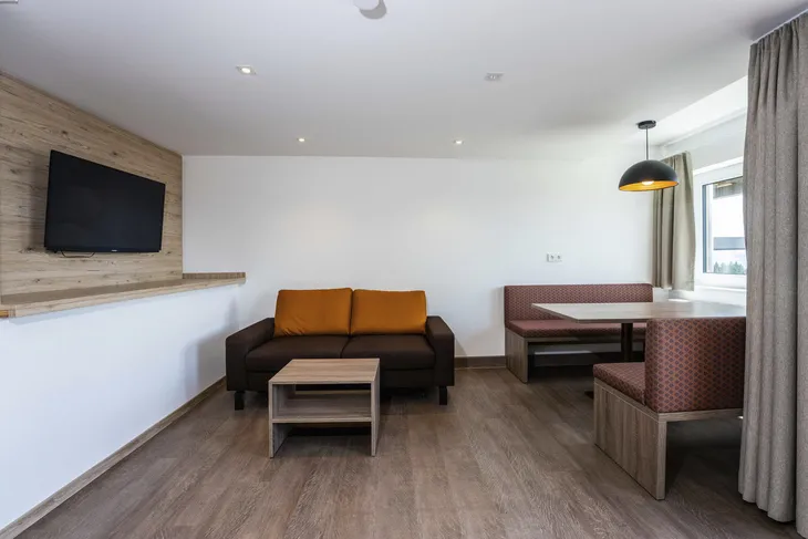 Sitzbereich mit Sofa, Tisch, TV und Fenster in modernem Raum.