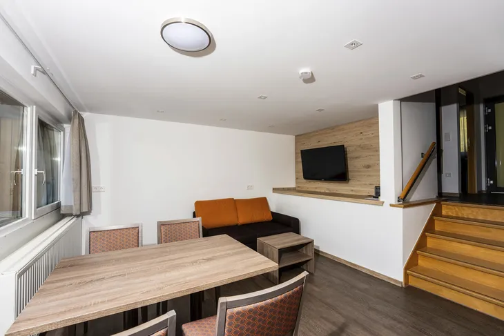 Wohnzimmer mit Tisch, Sofa, Fernseher und Treppe in moderner Einrichtung.