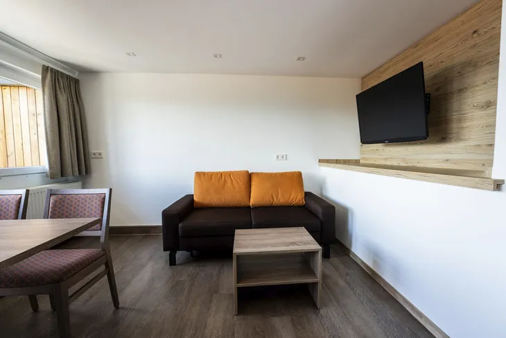 Wohnzimmer mit Sofa, Tisch, Stühlen, Fernseher an holzvertäfelter Wand.