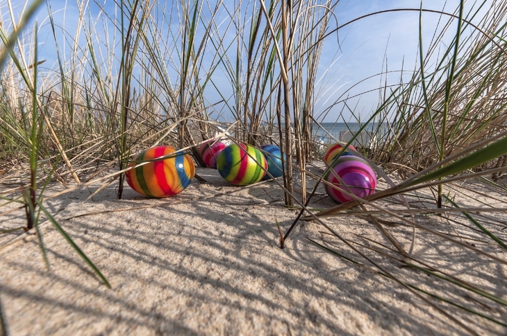 Bunte Ostereier in Sanddünen zwischen Grashalmen.