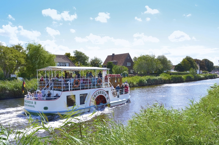 Bootsfahrt auf einem Fluss in Harlesiel, umgeben von grüner Landschaft.