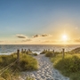 Sonnenuntergang am Strand mit Blick auf das Meer und einem sandigen Pfad.