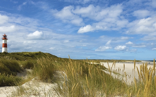 Leuchtturm auf einer Düne am Strand von Sylt unter blauem Himmel mit Wolken.