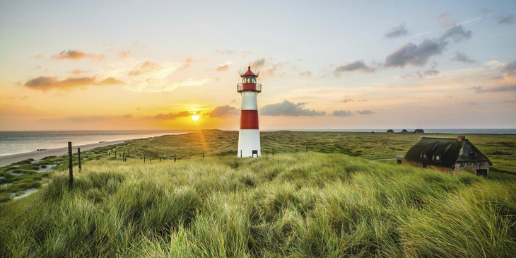 Leuchtturm und Haus auf einer Wiese bei Sonnenuntergang am Strand auf Sylt.