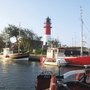 Boote im Hafen von Büsum vor einem Leuchtturm bei klarem Himmel.