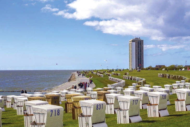 Viele Strandkörbe auf einer Wiese am Meer von Büsum, Hochhaus im Hintergrund, blauer, leichtbewölkter Himmel.