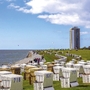 Viele Strandkörbe auf einer Wiese am Meer von Büsum, Hochhaus im Hintergrund, blauer, leichtbewölkter Himmel.