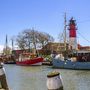 Blick auf den Museumshafen Büsum mit Schiffen und Leuchtturm bei klarem Himmel.