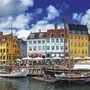 Bunte Häuser und Boote im Hafen von Nyhavn, Kopenhagen bei blauem Himmel.