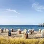 Strandkörbe am Timmendorfer Strand mit Seebrücke im Hintergrund und Seegras im Vordergrund, bei leichtbewölktem Himmel.