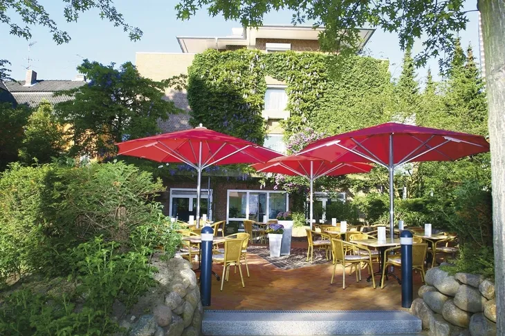 Außenbereich eines Cafés mit roten Sonnenschirmen und gelben Stühlen.