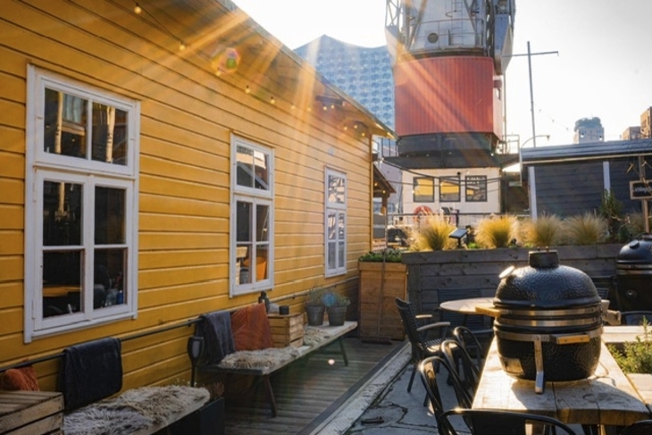Sonniger Innenhof mit gelbem Gebäude, Grill und Holzmöbeln.