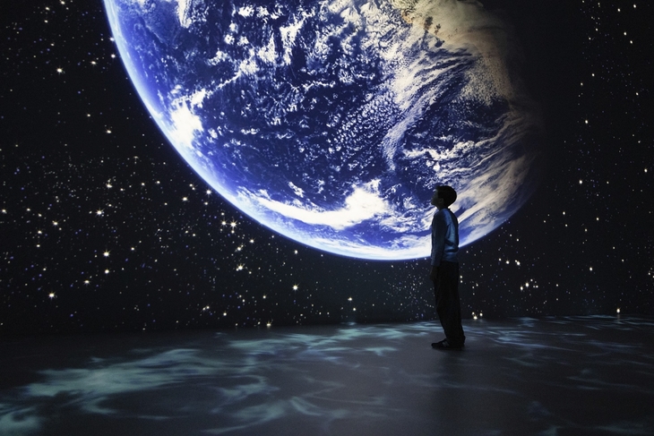 Person betrachtet Projektion des Planeten Erde in einem dunklen Raum.