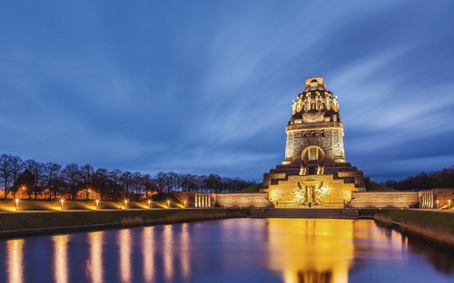 Völkerschlachtdenkmal in Leipzig bei Abenddämmerung, angestrahlt und reflektiert im Wasser.