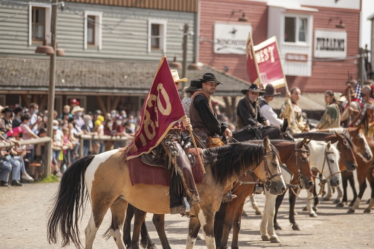 Reiterparade in einer Westernstadt mit kostümierten Personen und Zuschauern.