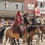 Reiterparade in einer Westernstadt mit kostümierten Personen und Zuschauern.