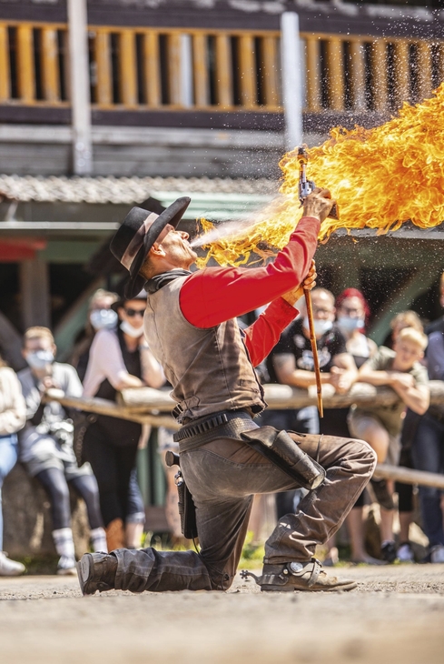 Mann in Westernkleidung führt eine Feuershow vor Publikum auf.