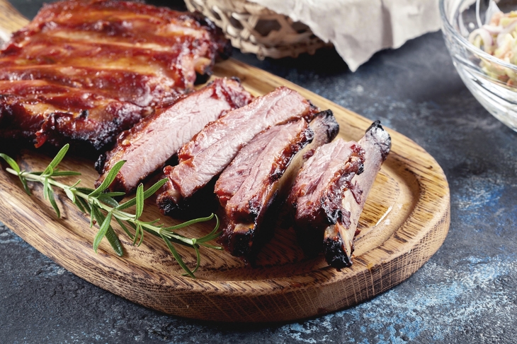 Gegrillte Spareribs auf einem Holzbrett, garniert mit einem Rosmarinzweig.