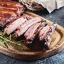 Gegrillte Spareribs auf einem Holzbrett, garniert mit einem Rosmarinzweig.