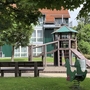 Spielplatz mit Spielturm und Wipptier sowie einer Holzbank vor einem Gebäude der Ferienanlage Braunlage.