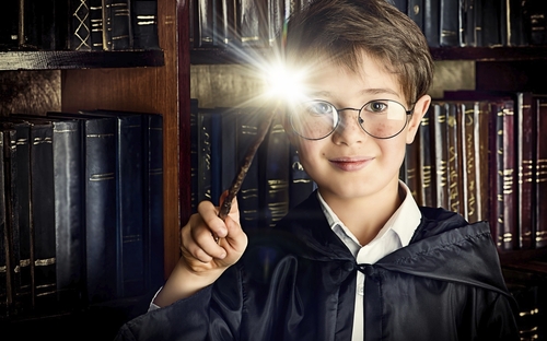 Kind mit Zauberstab vor Bücherregal, erzeugt magisches Leuchten.